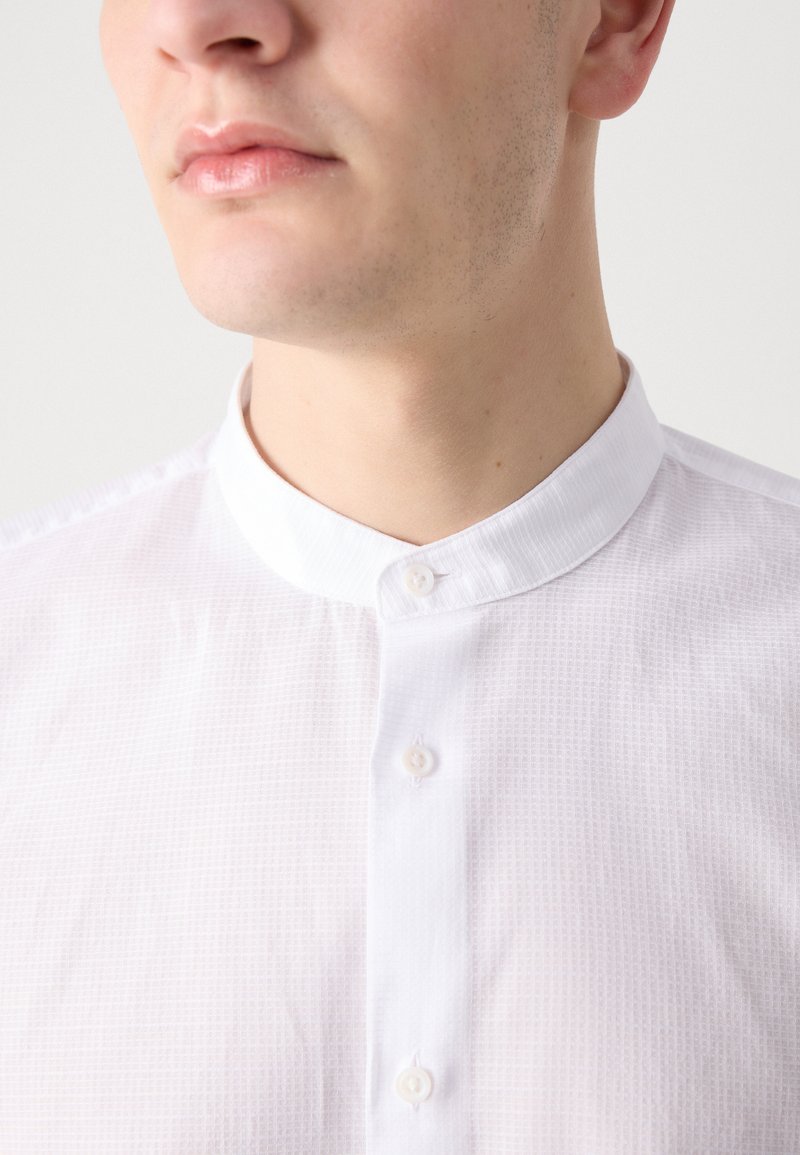Biała, teksturowana koszula z długim rękawem i stójką, z trzema guzikami z przodu. Gładki materiał z subtelnym wzorem siatkowym.