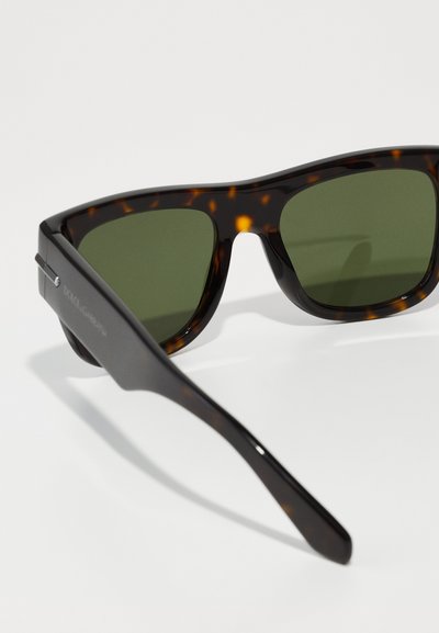 Tortoiseshell sunglasses with green lenses. Thick plastic frames feature a matte finish and a straight temple design with subtle branding.