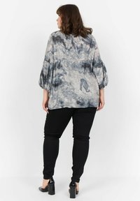 Halenka s dlouhými rukávy v šedém a černém tie-dye vzoru, spárovaná s černými úzkými džíny. Halenka má nafouknuté rukávy a volný střih.