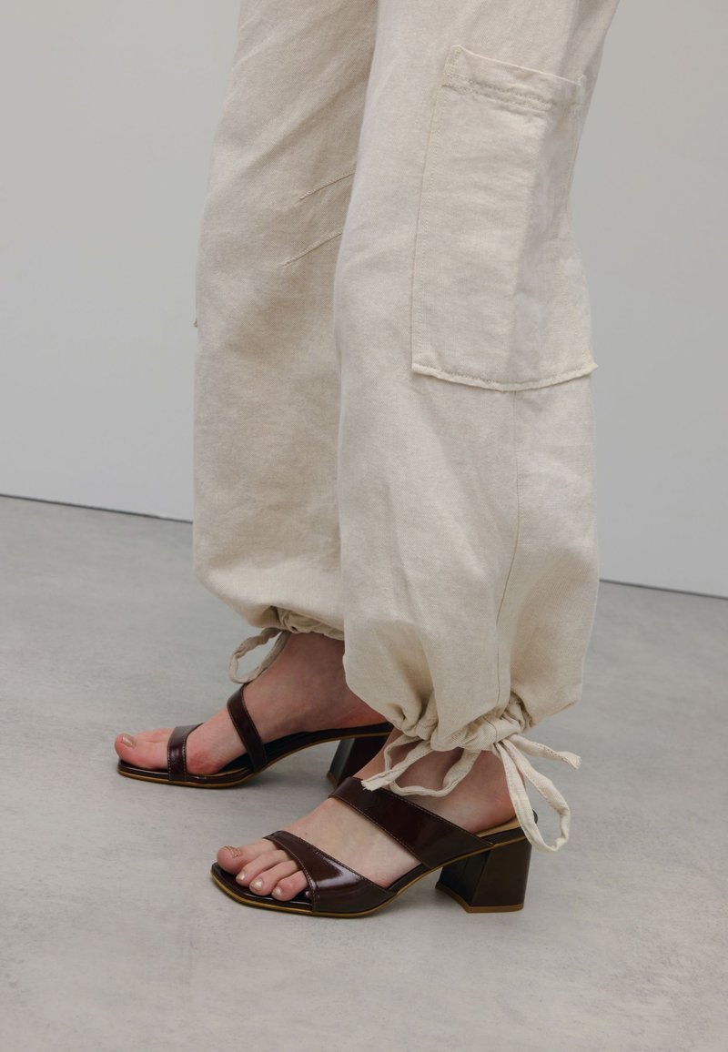 Beige linnen broeken metGathered ankles en zijzakken, gecombineerd met bruine sandalen met blokhak en twee brede banden.