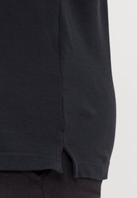 Närbild av mörk tygskjortas fåll med sidoklyvning som bärs över matchande byxor.