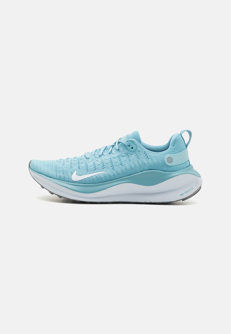 Vaaleansiniset Nike-juoksukengät, joissa on valkoinen swoosh-logo, teksturoitu neulottu päällinen, pehmustettu pohja ja vetotappi kannassa, esitettynä sivuprofiilissa.