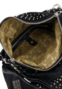 Czarna skórzana torba z metalowymi ćwiekami i zamkiem błyskawicznym, beżowe wnętrze w wzorki oraz wewnętrzna kieszeń zapinana na zamek z zatrzaskiem.