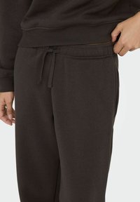 Mørkebrune joggere lavet af blødt stof har en elastisk talje med snøre, sidelommer og en afslappet pasform.