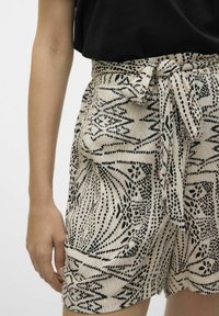 Shorts taille haute en tissu beige avec un motif abstrait noir, dotés d'une ceinture à nouer et de poches latérales pour plus de détails.
