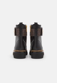 Czarne skórzane botki do kostki z brązowym wzorzystym materiałowym akcentem, złotymi suwakami i teksturowaną czarną gumową podeszwą z dekoracyjną złotą lamówką.