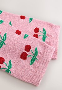 Vaaleanpunainen neulottu huivi, jossa on punaisia kirsikkakuviota vihreine lehtineen ja tunnultaan teksturoitu kangas.