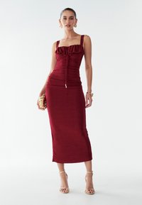 Burgundská priliehavá šaty s volánovým výstrihom, tenkými ramienkami a nariasenými detailmi. Hladká látka, po členky s elegantným strihom.