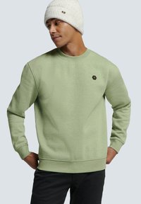 Groene sweatshirt met een ronde hals en ribgebreide manchetten, voorzien van een klein hexagonaal logo op de borst. Warme gebreide beanie in lichtgrijs.