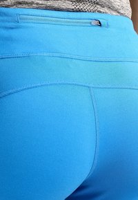 Niebieskie legginsy sportowe z gładkiego elastycznego materiału, dopasowane do ciała, z płaskim pasem w talii i małym detalem w postaci pętli z tyłu.