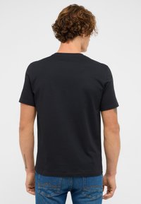 Czarna bawełniana koszulka z okrągłym dekoltem i krótkimi rękawami, charakteryzująca się gładką fakturą i minimalnym designem, noszona z niebieskimi dżinsami.