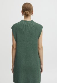 Grünes geripptes Strickkleid ohne Ärmel mit hohem Ausschnitt, das eine strukturierte Oberfläche und einen lässigen Schnitt hat, endet über dem Knie.
