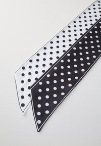 Écharpe en soie noir et blanc à pois, présentant de grands motifs circulaires, avec des côtés contrastés et une texture lisse. Les bords ont une fine bordure.