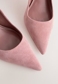 Een paar roze suède puntschoenen voor dames, weergegeven tegen een lichte achtergrond.