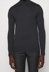 Pull à col roulé gris foncé en tissu doux, doté de manches longues et de poignets côtelés avec un détail de logo subtil à l'ourlet.