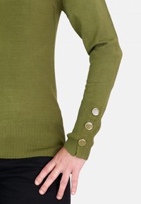 Suéter verde oliva hecho de un suave tejido de punto, con un diseño ajustado y puños acanalados que presentan tres detalles de botones metálicos.