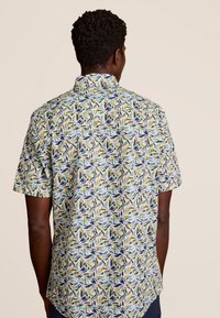 Korte mouwen shirt met een kleurrijk bladerenpatroon, met blauwe, groene en gele accenten op een lichte achtergrond. Gemaakt van katoen.