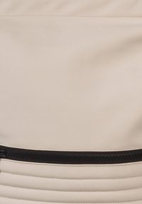 Beige synthetische tas met een gladde afwerking, voorzien van een horizontale zwarte rits. Getextureerde ribbelaccenten zorgen voor visuele interesse langs de basis.