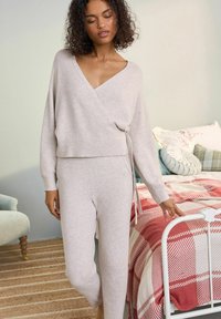 Svetlo bež ovitni pulover s skrajšanim robom in dolgimi rokavi, v kombinaciji z usklajenimi prilegajočimi hlačami. Mehka tekstura in minimalističen dizajn.