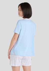 Top corto de manga corta color azul claro con escote redondeado y borde floral; combinado con pantalones cortos blancos que presentan un patrón floral colorido.
