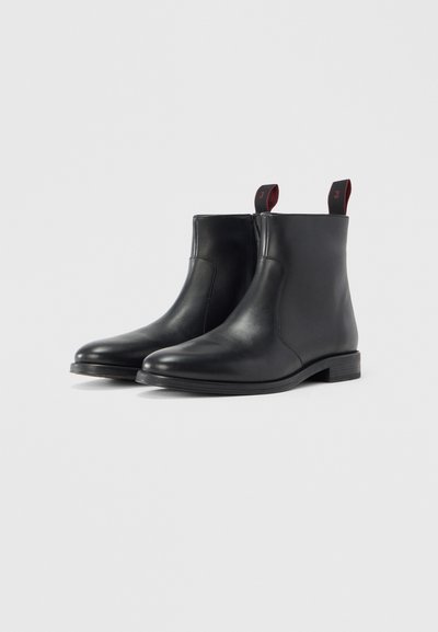 Botines de cuero negro con un diseño elegante, que cuentan con un tacón modesto y pestañas rojas en la parte trasera para facilitar su uso.