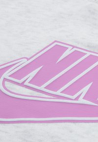 Το γκρι ύφασμα διαθέτει μεγάλο ροζ λογότυπο Nike με λευκά περιγράμματα. Η υφή φαίνεται απαλή και ελαφρώς με μοτίβο.