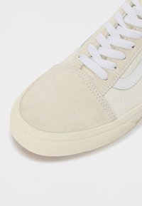 Beige semišové tenisky s bielymi šnúrkami a jemným brandingom. Majú štruktúrovanú gumovú podrážku a hladký kožený bočný pruh.