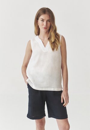 Haut sans manches en lin blanc avec un décolleté en V et des détails brodés au niveau du col, associé à un short bleu marine avec ourlet retroussé. Design simple, coupe décontractée.