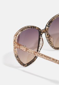 Oversized sunglasses with a transparent, speckled frame in brown and clear tones. Gradient lenses transitioning from dark to light. Metal accents.