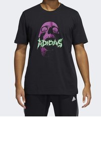 T-shirt en coton noir avec un motif graphique représentant un crâne en violet et vert, accompagné d'une police abstraite sous l'image. Manches courtes, coupe décontractée.