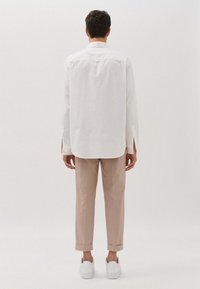 Witte blouse met klassieke kraag, lange mouwen en een rechte snit, gecombineerd met beige broek en witte sneakers.