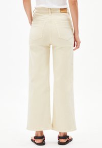Crème wijduitlopende jeans met een hoge taille, voorzien van twee achterzakken en een subtiele logo patch. Gemaakt van zacht denim met een gladde textuur.
