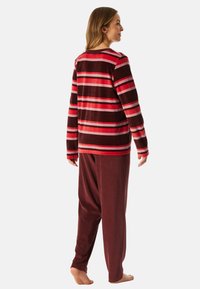 Conjunto de loungewear a rayas rojas y marrones, que incluye una parte superior de manga larga con cuello redondo y pantalones a juego con cinturilla elástica. Textura suave.