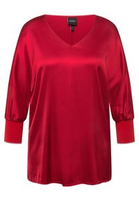 Chemise en satin rouge avec un col en V, des manches bouffantes 3/4 et des poignets rouges contrastants. Texture lisse avec un léger lustre.
