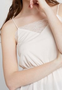 Camisola rosa chiaro con scollo ornato di pizzo, spalline sottili e vita arricciata, realizzata in un morbido tessuto testurizzato.