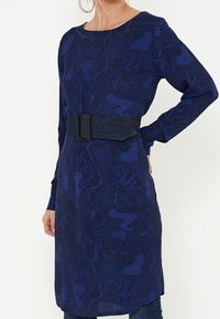 Long-sleeve navy dress with a floral pattern, featuring a denim belt at the waist and side slits for ease of movement.