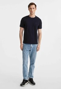 Granatowa bawełniana koszulka z krótkim rękawem, okrągłym dekoltem i małym teksturowanym logo. Połączona z jasnoniebieskimi dżinsami i czarnymi sneakersami.