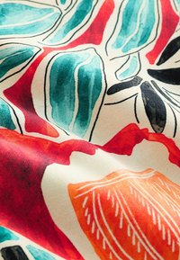 Színes szövet absztrakt levélmintákkal, türkiz, piros, narancs, fekete és fehér színekben, textúrát és hajtásokat mutatva.