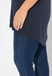 Marinblå topp med kort ärm och rundad nederkant, kombinerad med mörkblå skinny jeans. Den släta tyget och den figurnära designen framhäver siluetten.