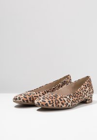 Une paire de chaussures à talons bas pour femmes avec des pointes effilées et un motif léopard noir et orange sur une surface blanche.