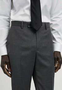 Pantaloni gri, ajustați, dintr-un material texturat, cu închidere prin buton, buzunare pentru curea și detalii plisate pe partea din față.