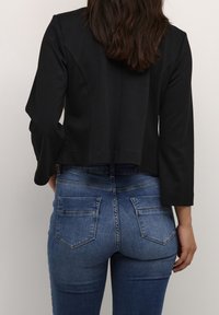 Svart kort jacka med långa ärmar, parat med blå denimjeans med bakfickor och ett urblekt mönster. Standard sömnadsdetaljer är synliga.