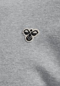 Schwarz-weiß besticktes Bienen-Patch auf grauem Strickstoff-Hintergrund, zentriert und deutlich sichtbar.