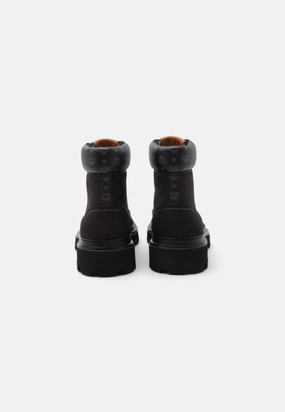 Paire de bottines noires avec col rembourré présentant un motif monogramme subtil, vues de dos sur fond blanc.