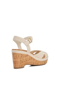 Beige wedge sandal with cork platform and textured fabric straps, featuring a gold-tone buckle and cross-strap design for secure fit.