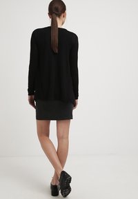 Suéter negro de manga larga con un corte relajado, falda gris texturizada y calzado negro. Diseño sencillo sin patrones visibles ni acentos.