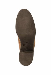 Zapato de ante marrón con suela de goma texturizada, que presenta una punta redonda y un logotipo discreto en la suela exterior. Diseño simple y funcional.