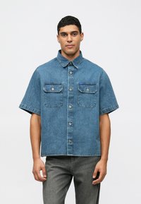 Kortärmad denimskjorta i ljusblått med två bröstfickor, knapplist framtill och krage. Slät textur och avslappnad design.