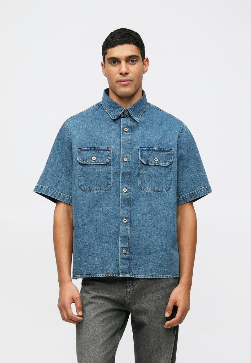 Kortärmad denimskjorta i ljusblått med två bröstfickor, knapplist framtill och krage. Slät textur och avslappnad design.