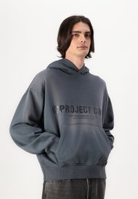 Grauer Kapuzenpullover mit einer Fronttasche, ausgestattet mit einem schwarzen Logo und Textdruck. Weicher Stoff, lockerer Schnitt, gerippte Bündchen und Saum.